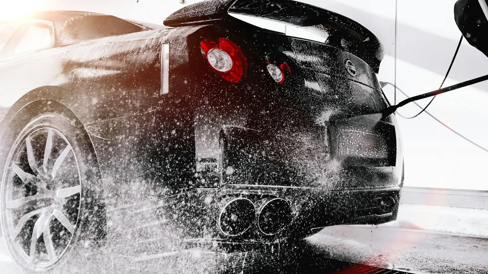 Sportwagen wird von hinten mit dem Hochdruckreiniger abgespült, Wasser spritzt im Gegenlicht